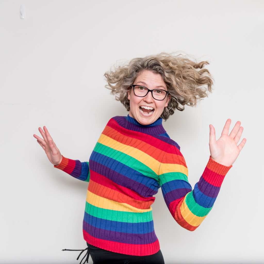 Nez jumping in a bright rainbow jumper smiles at the camera